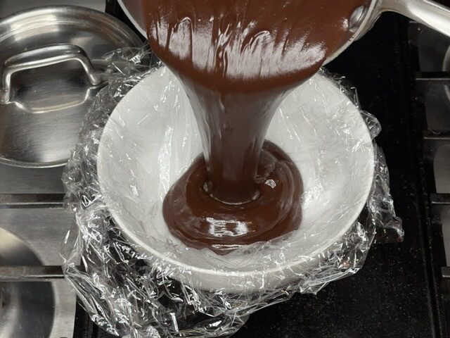 Pouring Dark Chocolate Godiva Truffles filling into plastic wrap lined bowl.