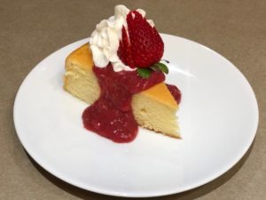 Strawberry Rhubarb Sauce on Lemon Chiffon Cake. Garnished with whipped cream and strawberry fan.