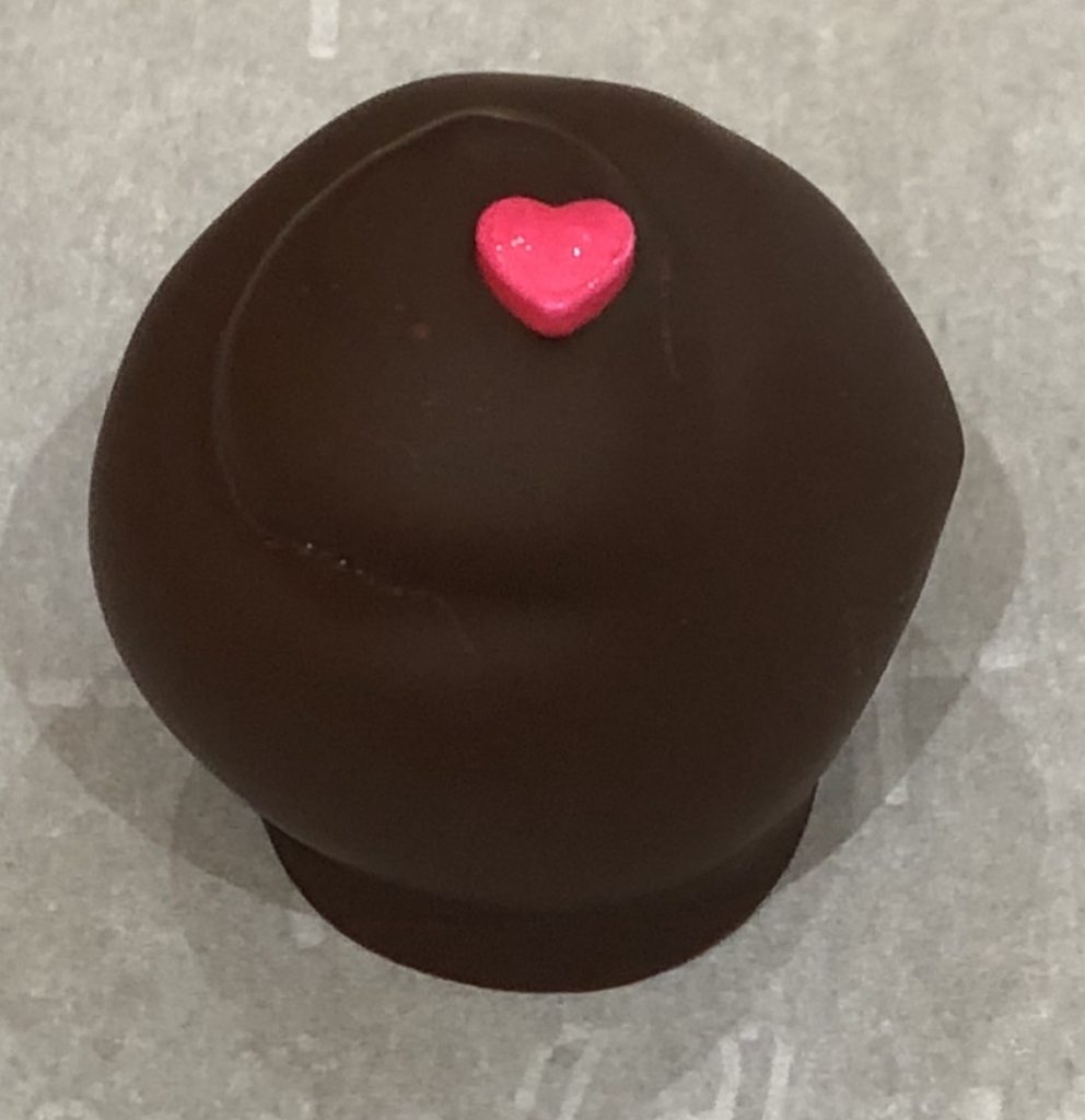 Photo of Cinnamon Chocoate Truffle that is coated with Dark Chocolate with bright red candie heart garnish.